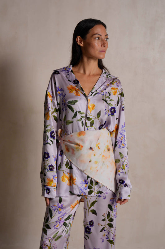Woman wearing a tropical floral silk satin pajama set against a plain background