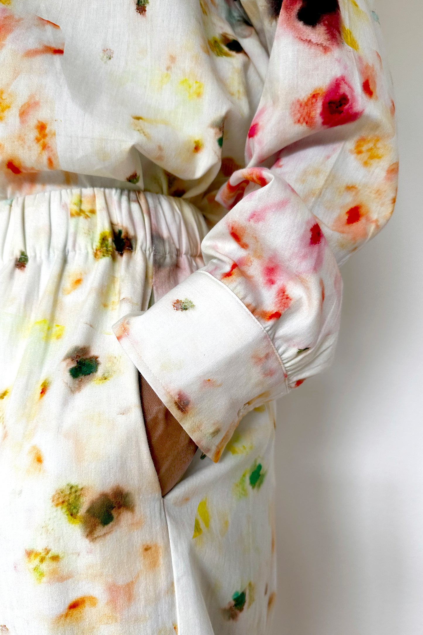 Close-up of a person wearing a matching loungewear set with a colorful, abstract floral pattern. Their hand is casually placed in their pants pocket, showcasing the elastic waistband and gathered fabric on the sleeve cuff. The background is plain and white.