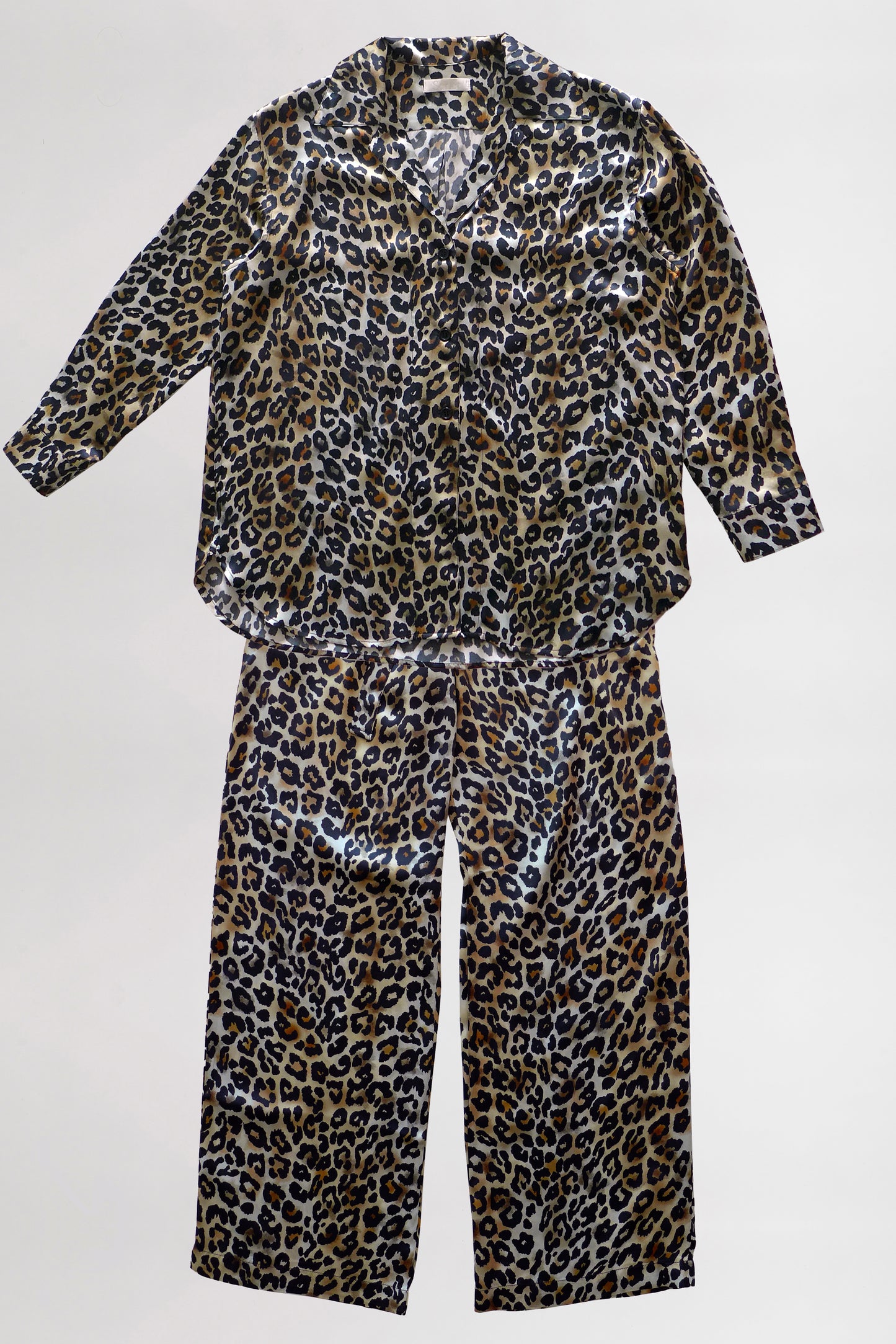 A leopard print loungewear set, featuring a matching oversized shirt and pants on a neutral background. The fabric has a shiny finish, giving it a sleek look.