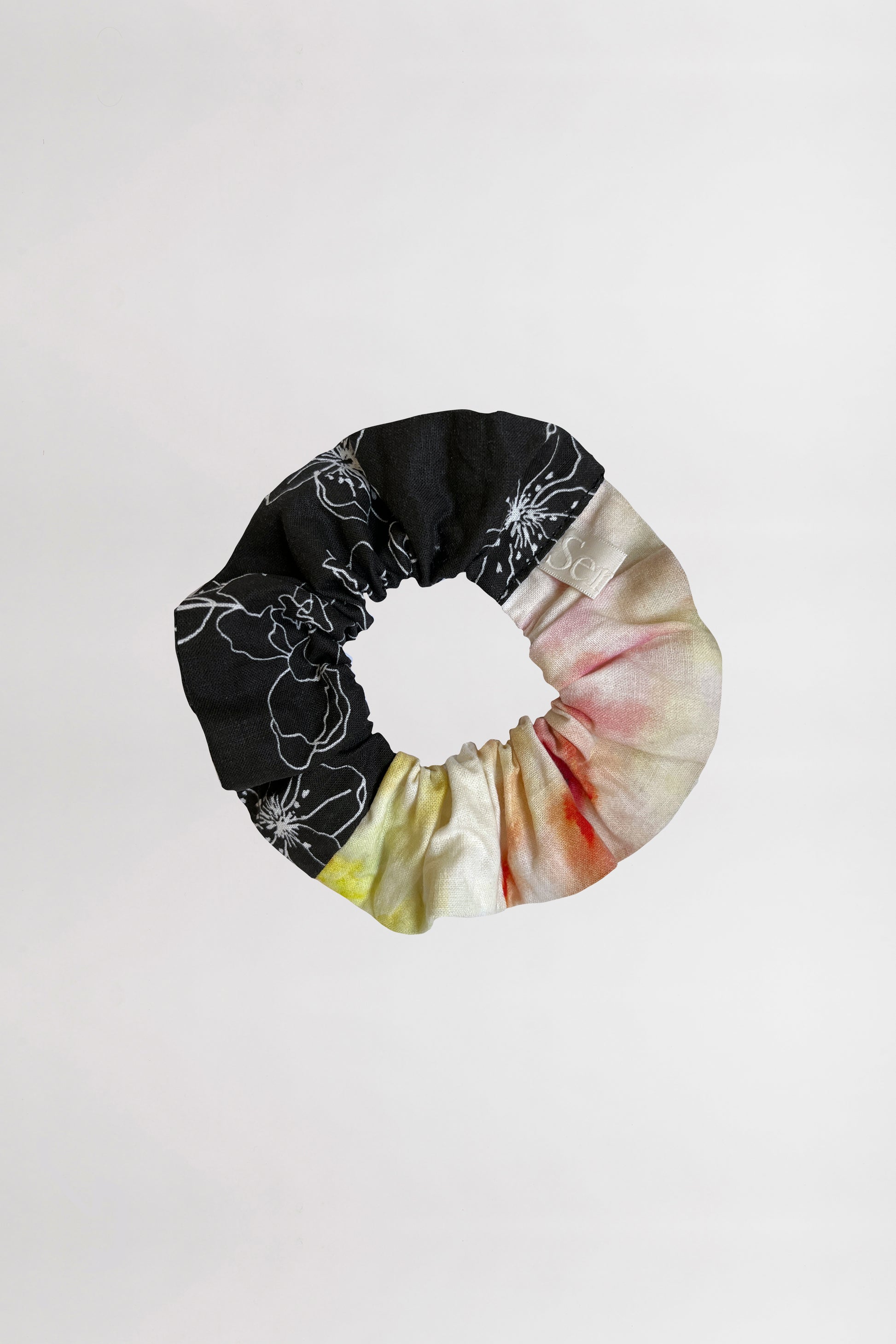 Front view of a scrunchie featuring two unique patterns – one with white linear flowers on a black background, and the other with a colorful abstract design – crafted from leftover fabrics, set against a neutral backdrop.