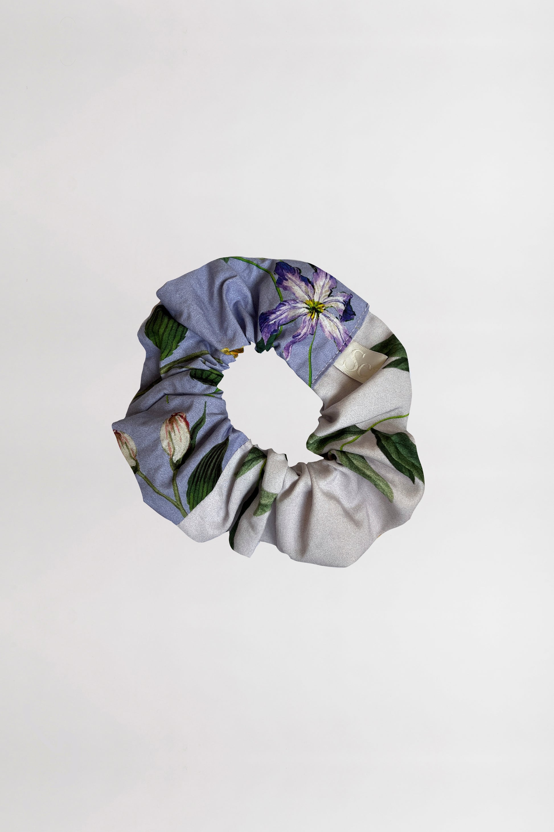 Foreground perspective of a scrunchie accentuating two floral prints, with one displaying varying shades of lilac backgrounds crafted from leftover fabrics against a neutral backdrop.