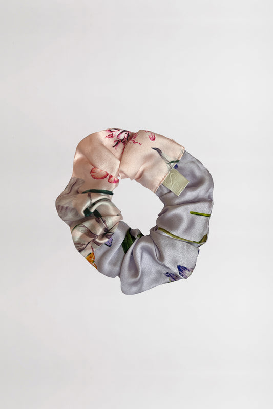 A silk satin scrunchie with two different floral patterns on a neutral background. The fabric features light pastel colors and delicate flower designs, giving it a soft and elegant appearance, made from left over fabric.