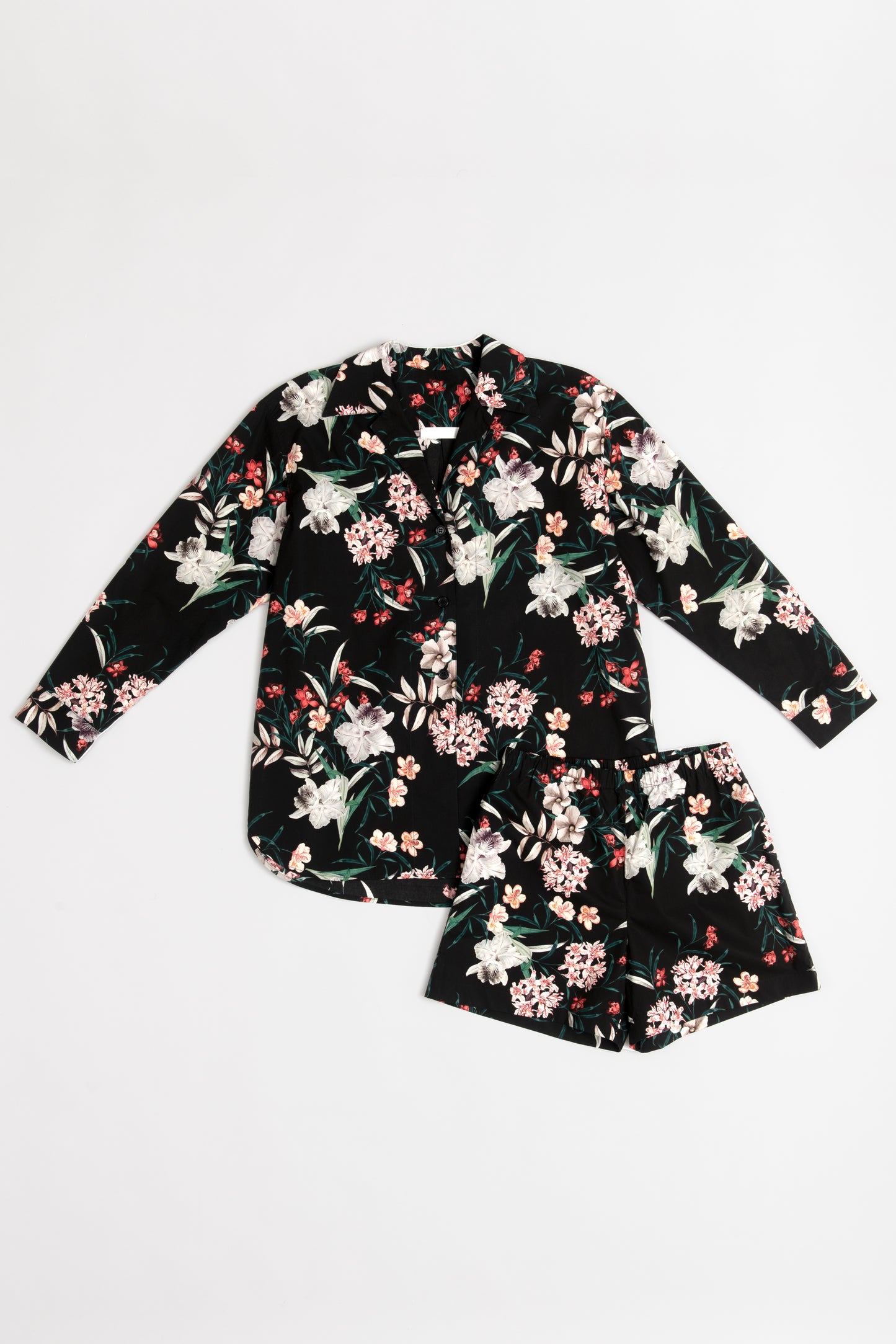 A black long-sleeve loungewear set with a tropical flower print featuring green leaves and white, pink, and red flowers. The shirt and shorts are made of a soft, flowing fabric and arranged neatly on a white background.