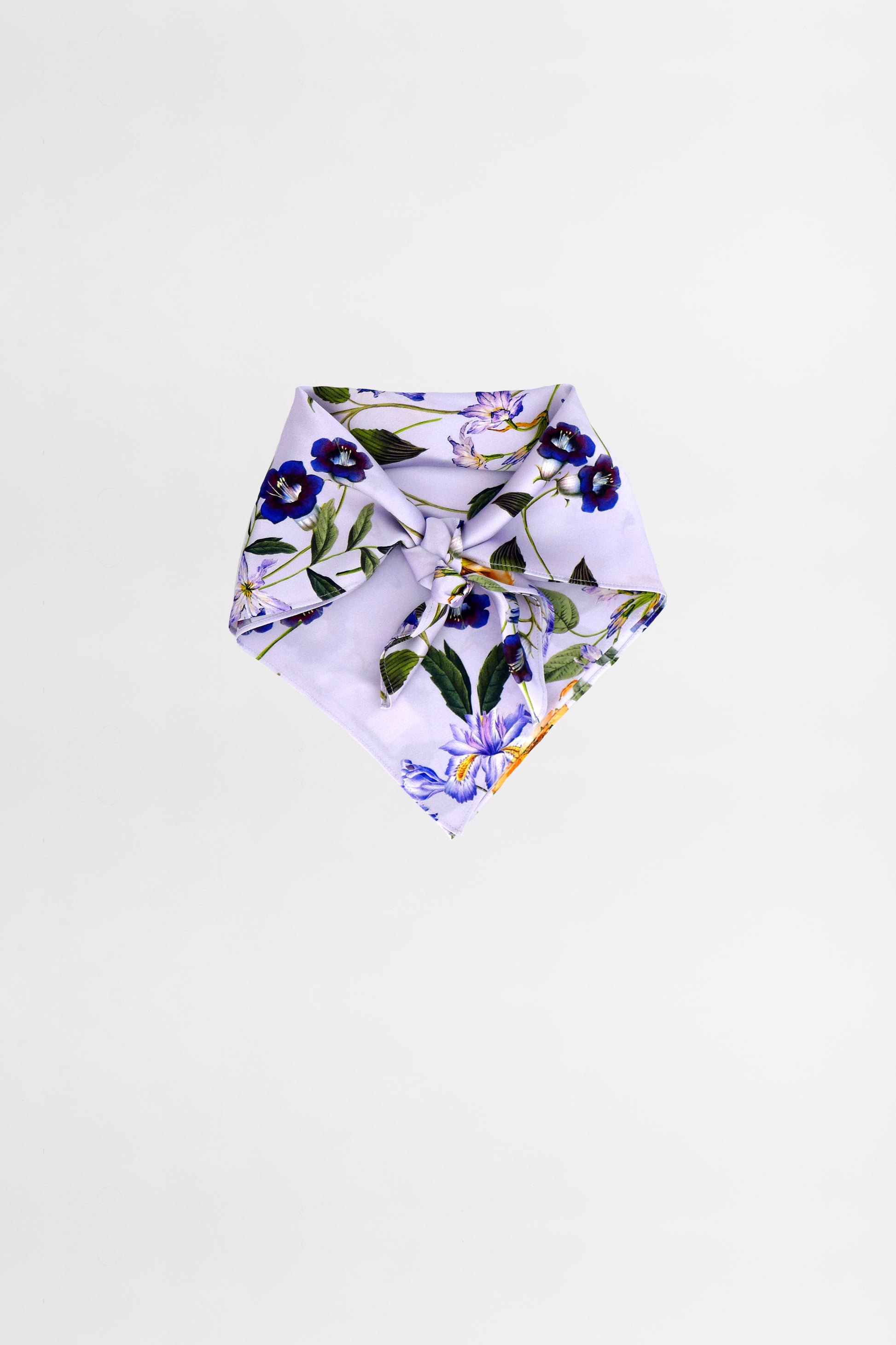 A neatly folded, floral-patterned foulard featuring purple and yellow flowers with green leaves on a light background. The scarf is positioned against a plain white backdrop.