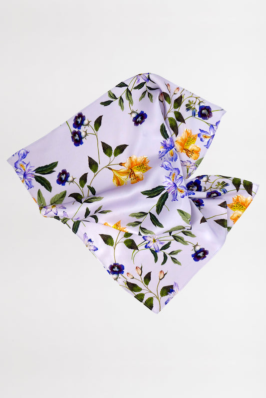 A square white fabric adorned with a floral pattern featuring yellow and purple flowers, along with green leaves. Made from leftover fabric, it has a soft, flowing appearance, suggesting it is lightweight and delicate.