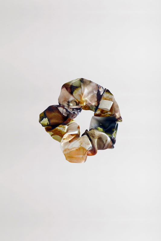 A hair scrunchie made from leftover silk satin fabric, showcasing a marbled design with shades of brown, beige, and green against a plain white background.