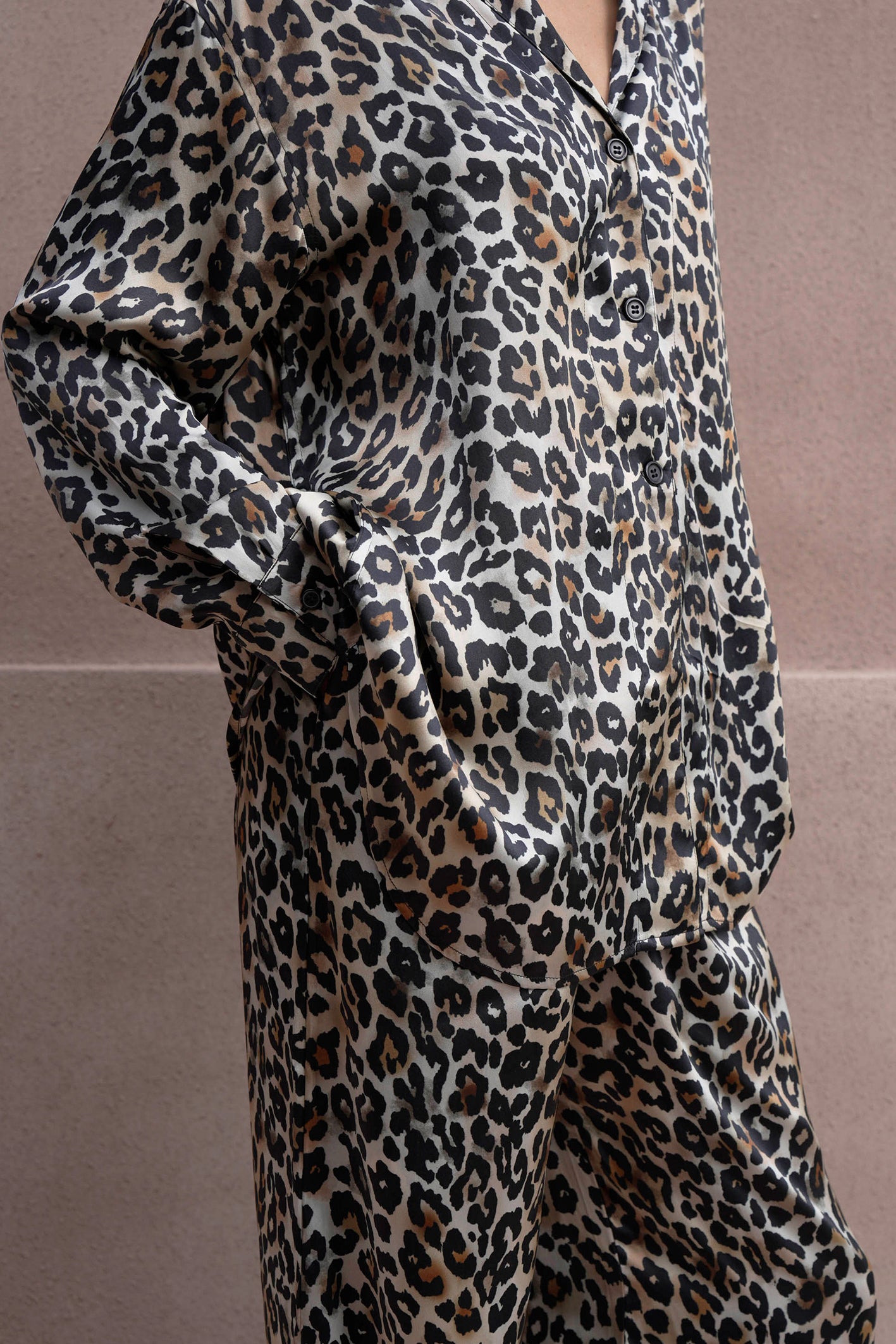 A person wearing a silk satin loungewear set with a matching shirt and pants in a bold leopard print. The relaxed fit and glossy fabric enhance the luxurious feel, while the person casually places one hand in their pocket.