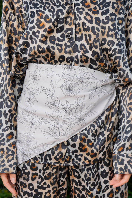 A person wearing a leopard print shirt and pants with a linear floral patterned in black and white, foulard over the loungewear.