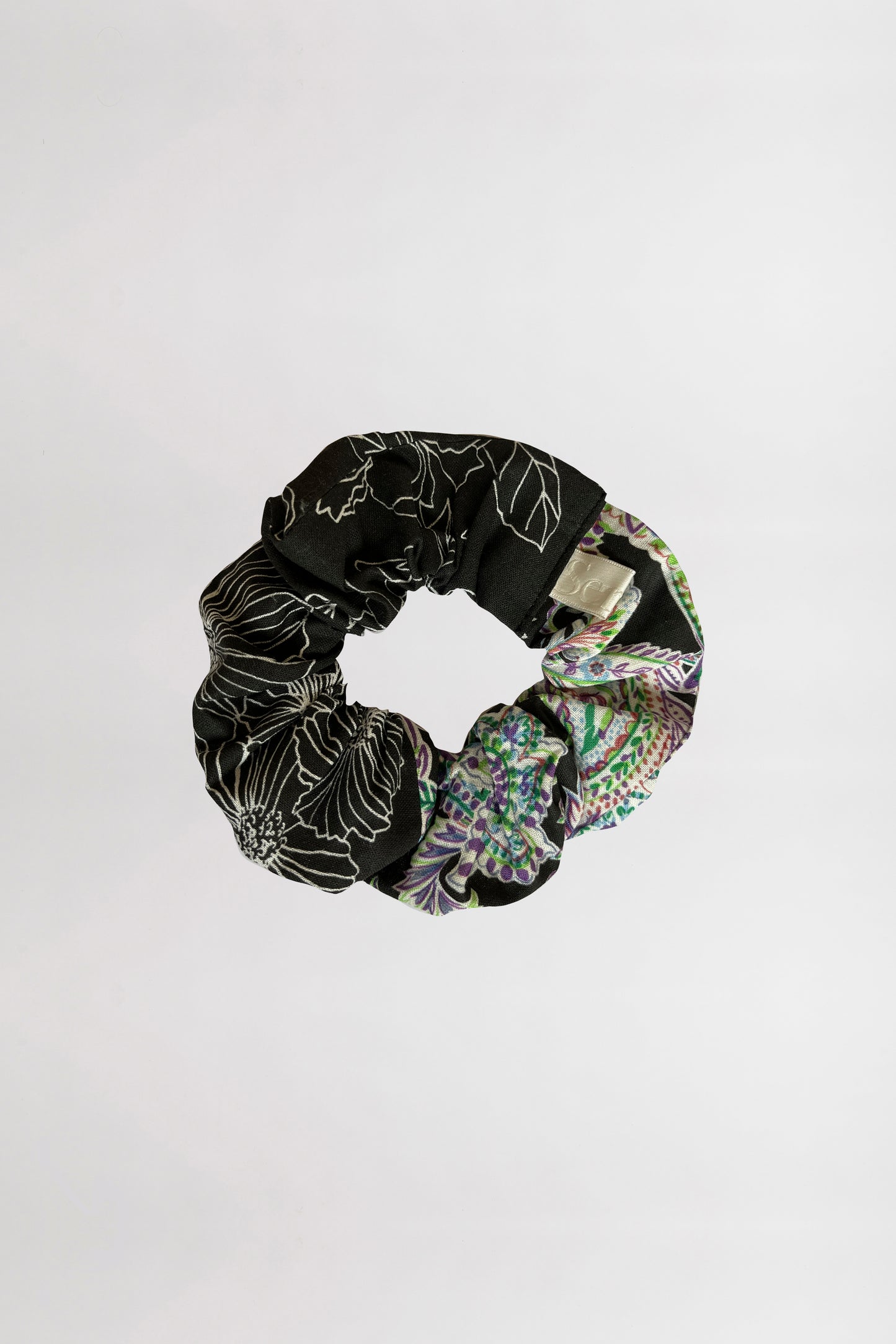Scrunchie, one black with floral pattern and one multicolored, on a white background.