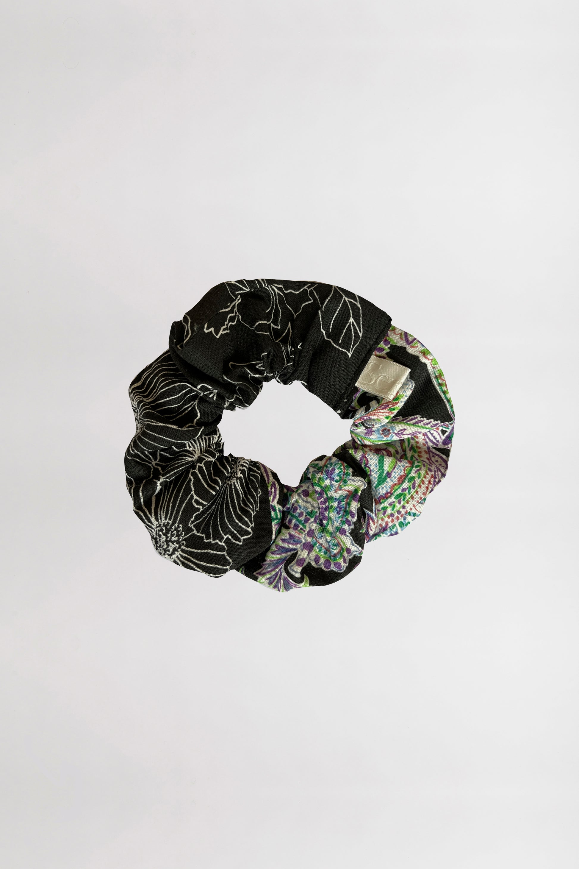 Scrunchie, one black with floral pattern and one multicolored, on a white background.