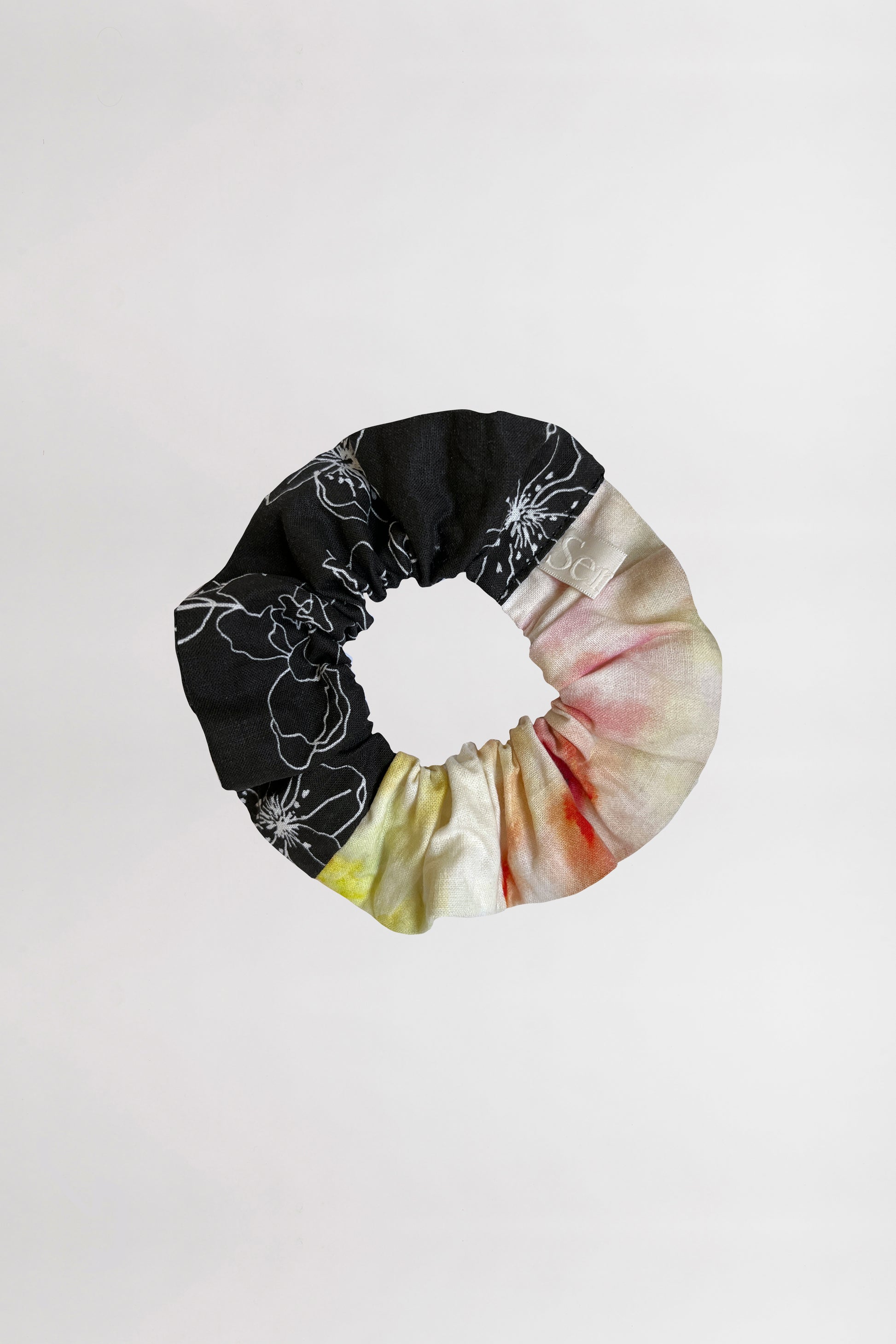 Front view of a scrunchie showcasing two distinct prints – one floral, the other abstract – crafted from leftover fabrics against a neutral background.
