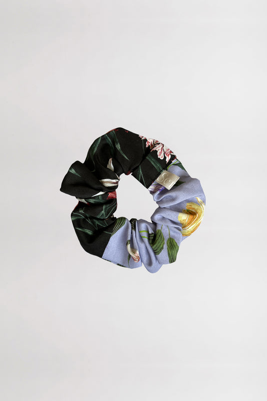 Front view of a scrunchie highlighting two floral prints, one featuring a black background and the other a lilac hue, crafted from leftover fabrics against a neutral backdrop.